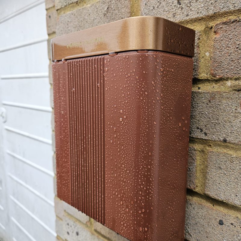 Copper Simpson and Partners charger, beaded with rain, on the brick beside the garage door